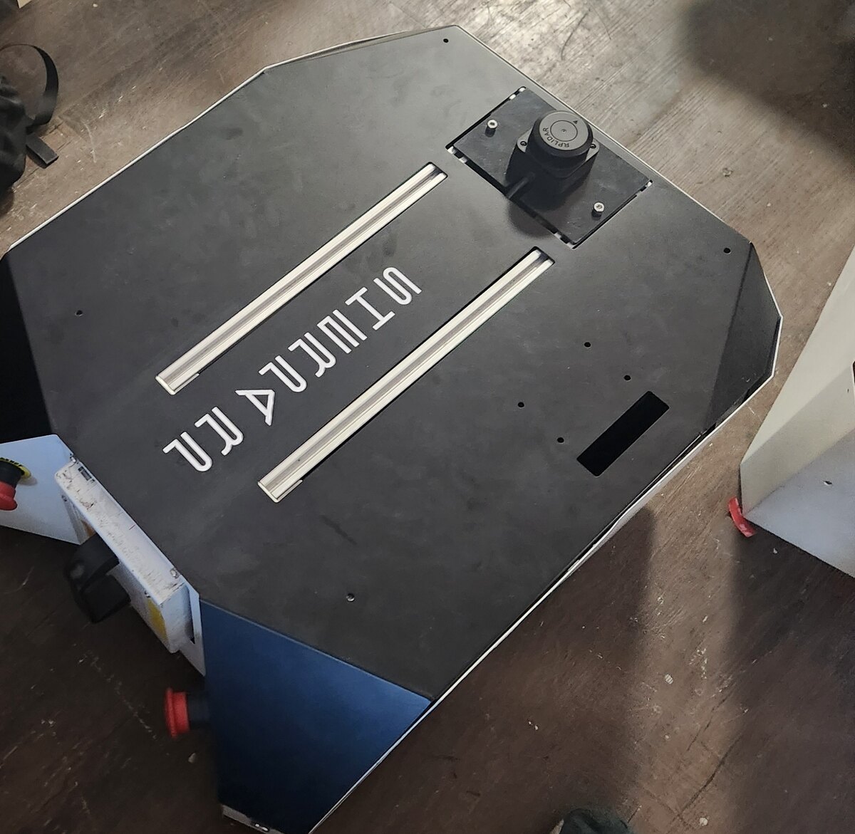 The AMR photographed from above on a workshop floor, showing the top deck, sensor mount and hazard markings.