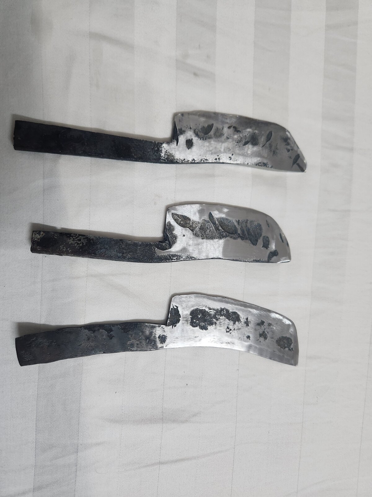 A finished chef's knife with a pale burl wood handle, blade left dark with forge finish, photographed on white paper.