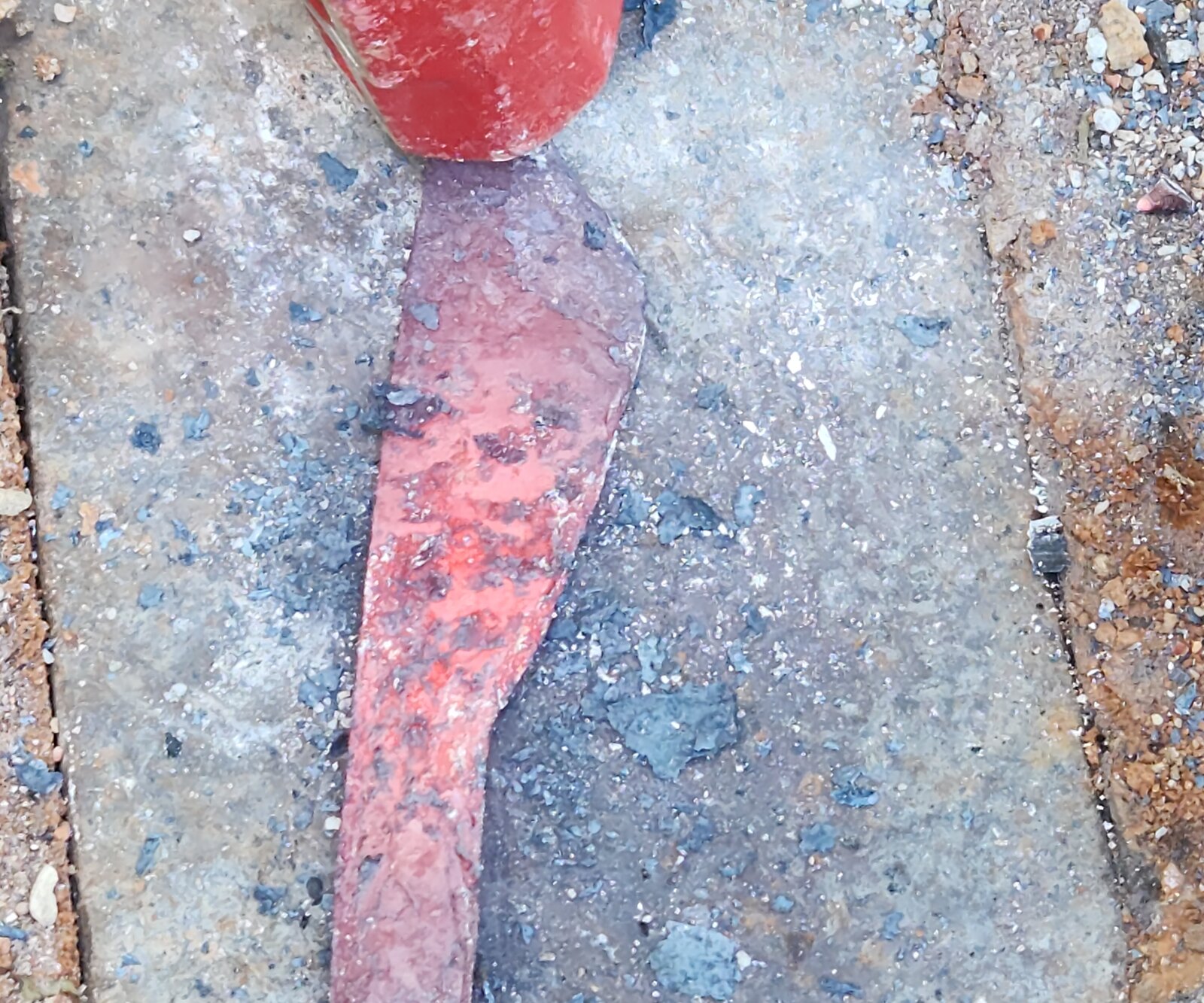 A blade at forging heat, glowing dull orange-red, lying on a stone slab with a sledgehammer resting beside it.