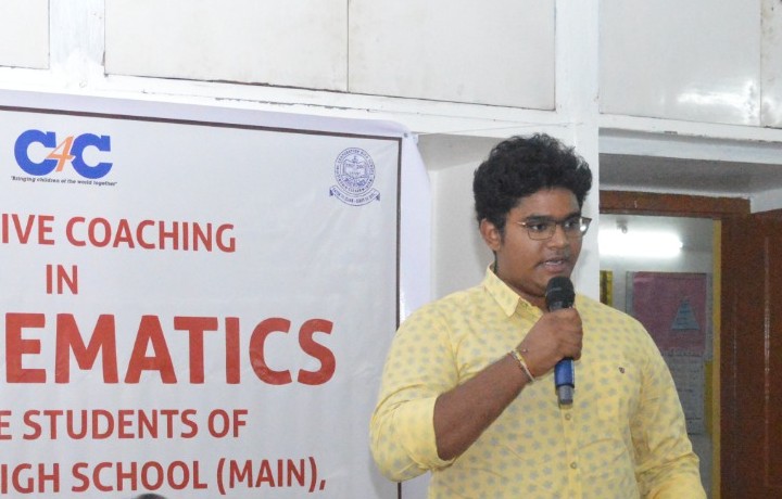 Abhiram speaking into a microphone beneath a banner reading 'Intensive coaching in mathematics for the students of Municipal High School (Main), Kadapa', with the Children for Children logo.