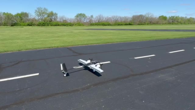A twin-boom fixed-wing UAV accelerating down a paved runway, grass either side, clear sky.