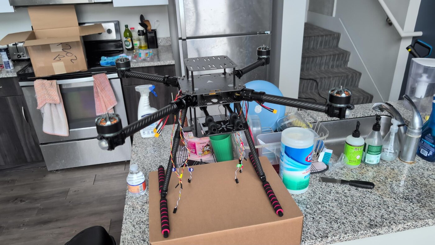 A carbon-fibre quadrotor frame part-assembled on a kitchen counter, arms and motors fitted, wiring loom laid out around it.