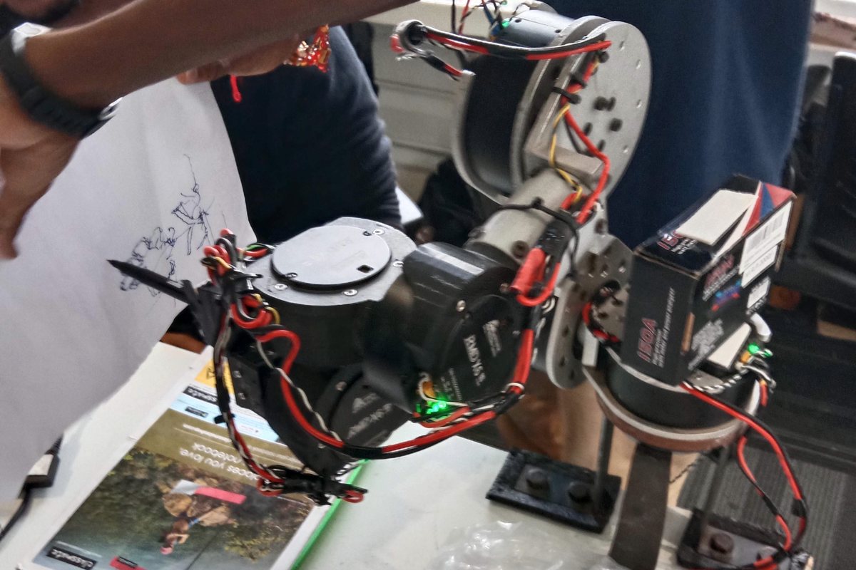 A multi-axis robot arm on a bench at the robotics shop, joints and wiring exposed.