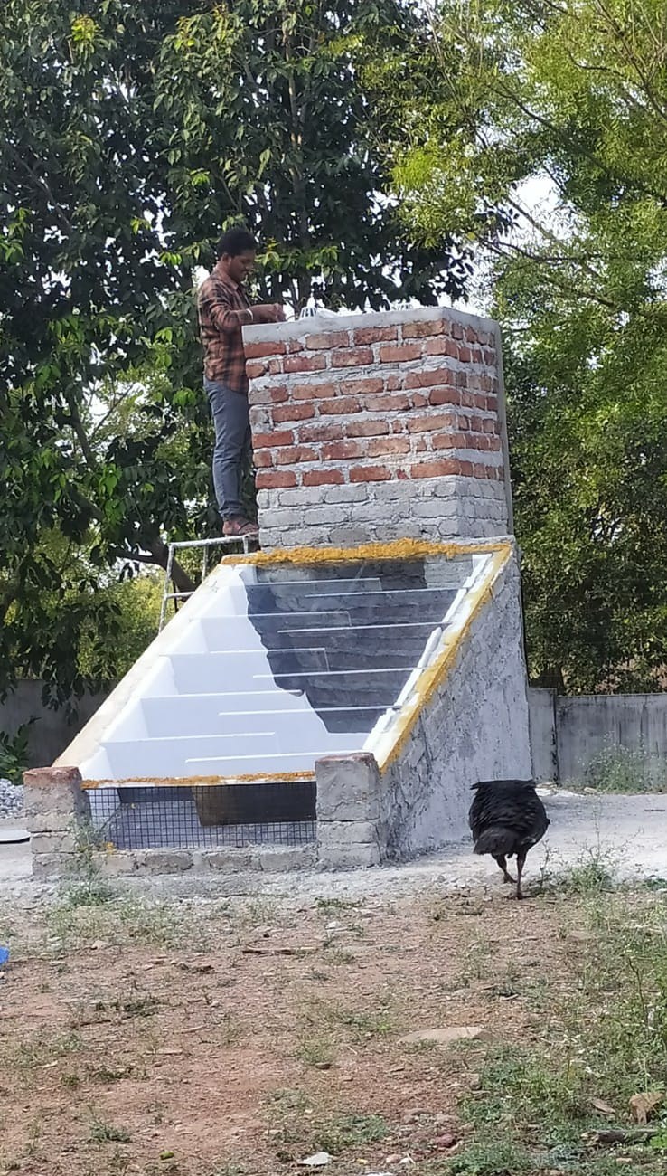 A dryer under construction: brick drying chamber part-built, the glazed collector with its dark zigzag slats already in place below, a mason standing on the chamber top, mesh air inlet at the base.